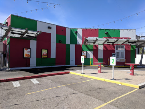 A colorful fast-food restaurant with a red and green exterior and two drive-thru order stations.